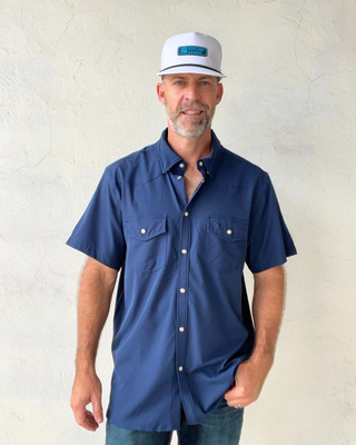 Man wearing a blue shirt and white cap against a plain background