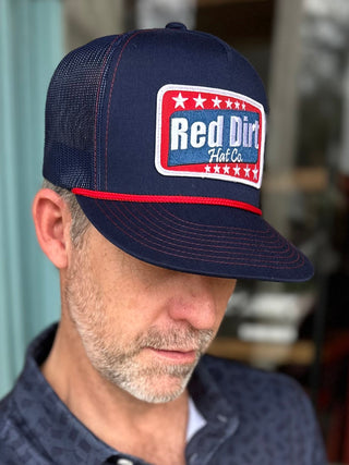 Man wearing a navy cap with a logo and a matching polo shirt, sitting outdoors.