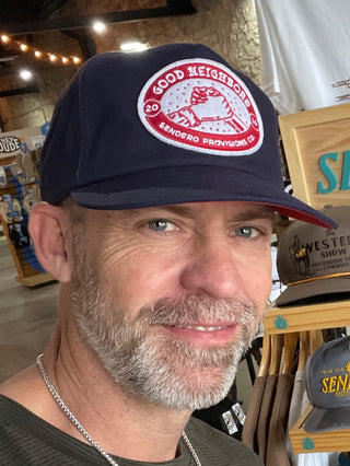 Man wearing a navy cap with a 'Good Neighbors' logo in a store setting
