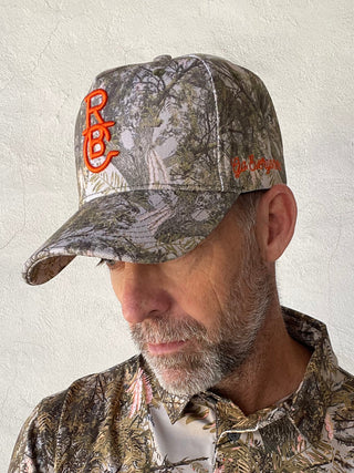 Person wearing camouflage clothing and a hat with a brand logo on a light background