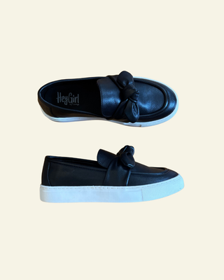 Pair of black loafers with a bow on a beige background