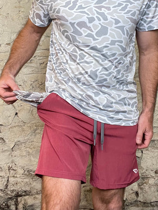 Person wearing a patterned shirt and maroon shorts on a textured surface