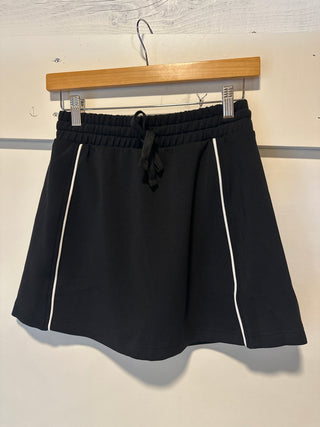 Black skirt with white trim on a hanger against a light background