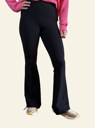 A person wearing black twist and flare crossover leggings with a pink top, standing against a white background.