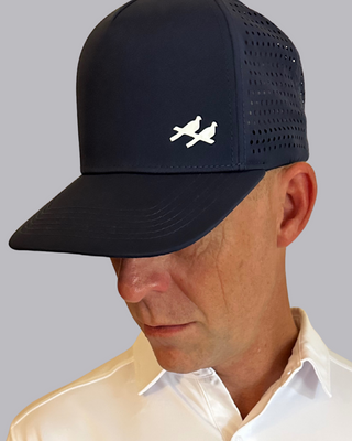 Man wearing a white polo shirt with black and blue pattern and a black cap with a logo on a gray background