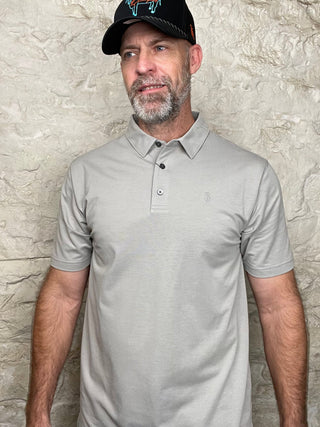 Man wearing a gray polo shirt and black cap against a textured wall.