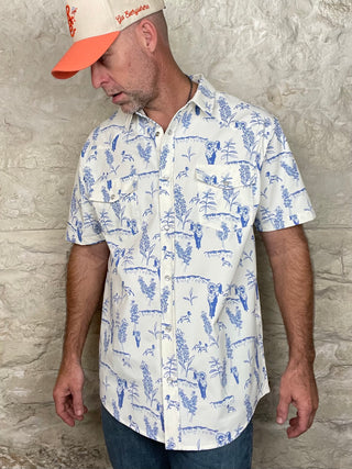 Man wearing a white shirt with blue patterns and an orange cap against a stone wall.