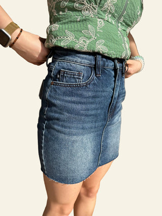 Person wearing a green top and blue denim shorts sitting on a stone floor.