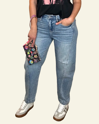 Person wearing blue jeans and white sneakers holding a colorful clutch on a plain background