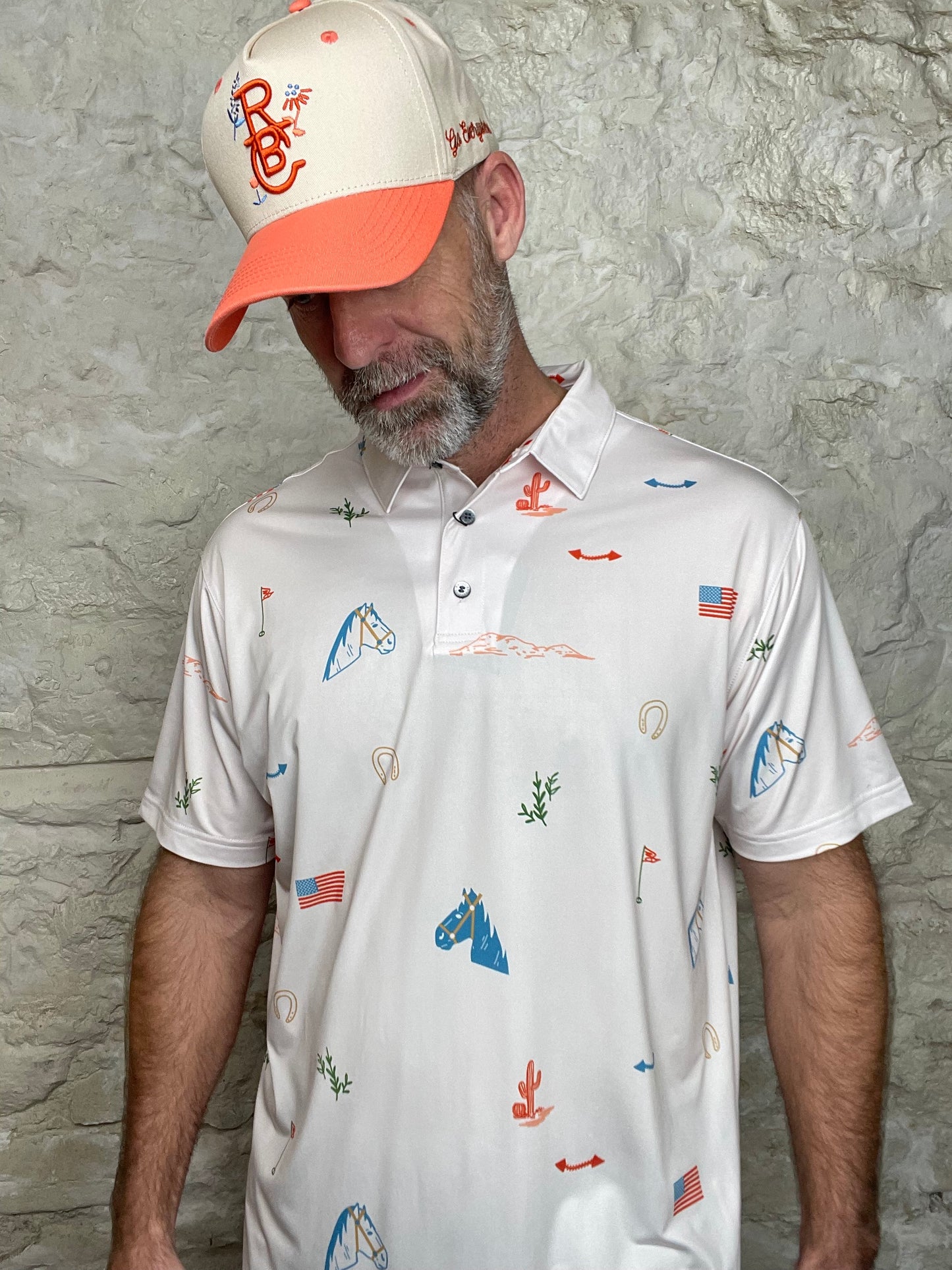White polo shirt with colorful graphics worn by a person against a stone wall background