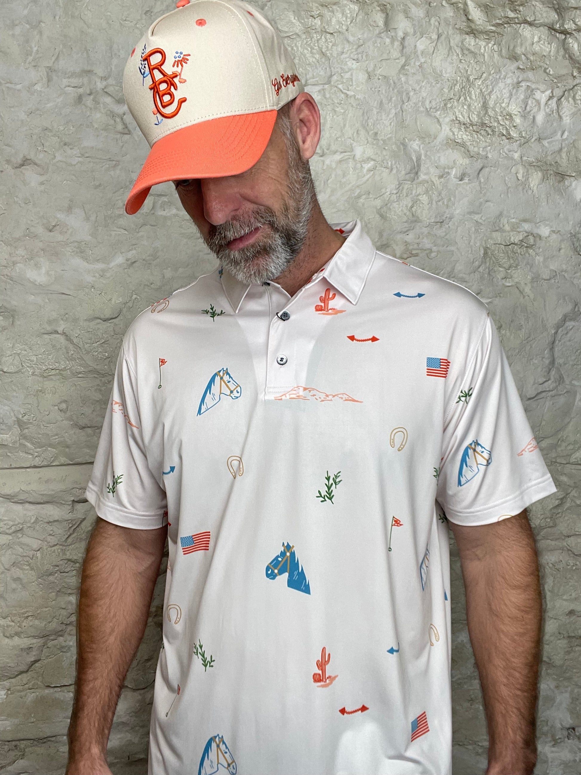 White polo shirt with colorful graphics worn by a person against a stone wall background