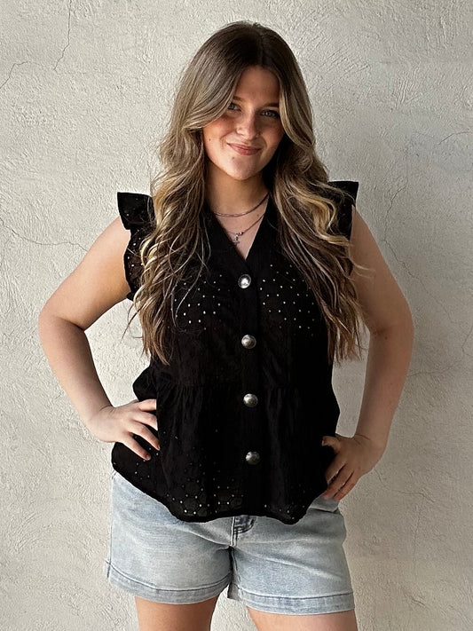 Woman wearing a black sleeveless top with silver buttons against a beige wall