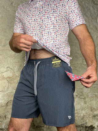 Person wearing a patterned shirt and blue shorts with a visible brand tag, standing on a stone surface.