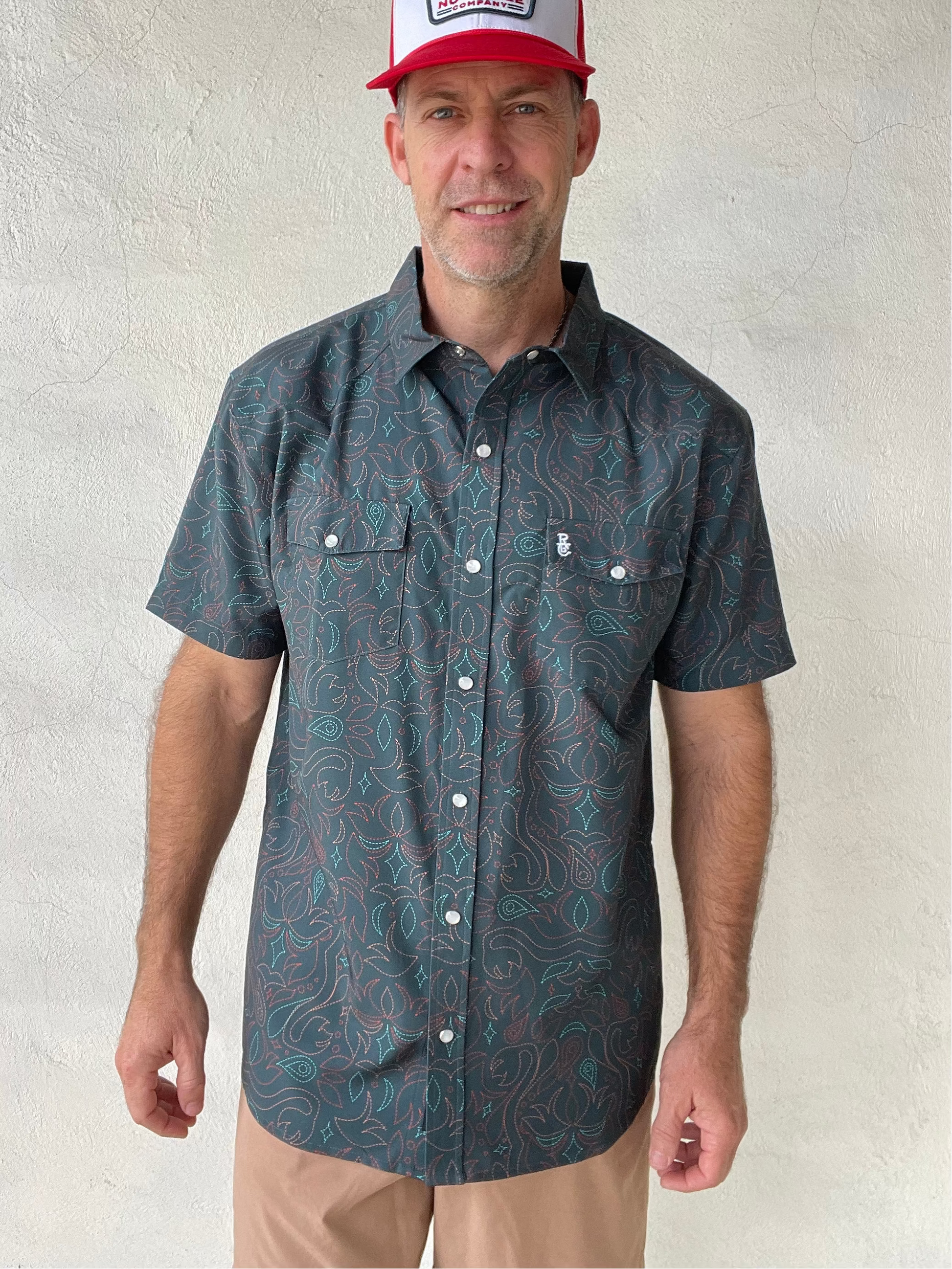 Man wearing a patterned short-sleeve shirt and a cap against a plain background