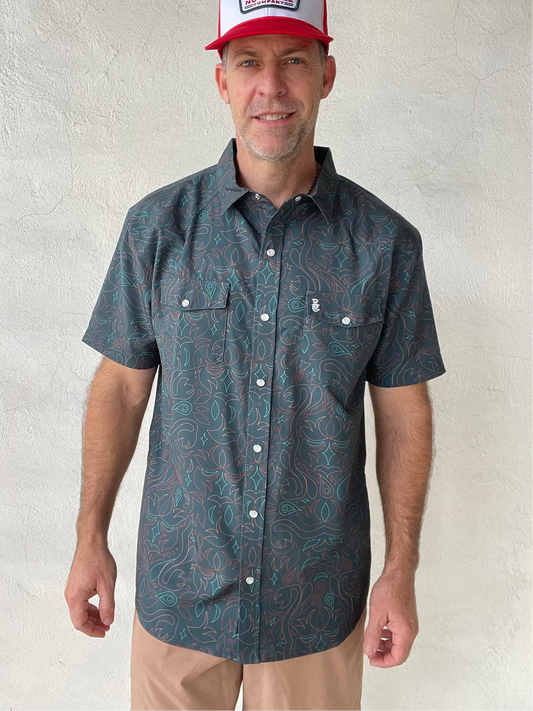 Man wearing a patterned short-sleeve shirt and a cap against a plain background
