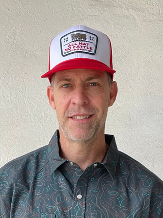 Man wearing a patterned short-sleeve shirt and a cap against a plain background