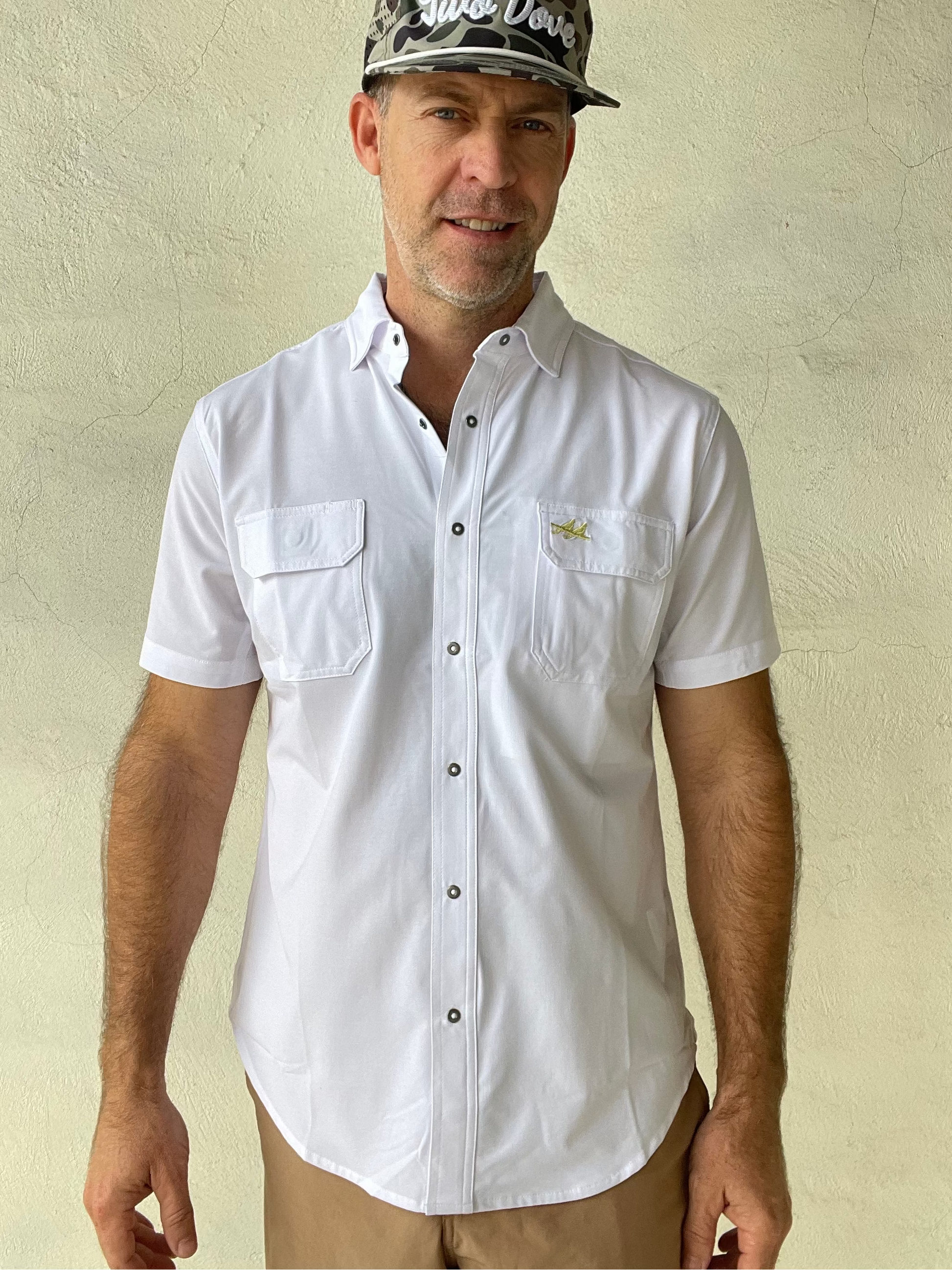 Man wearing a white shirt and camouflage cap against a beige wall