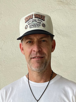 Man wearing a white t-shirt with text and a cap, standing against a plain background