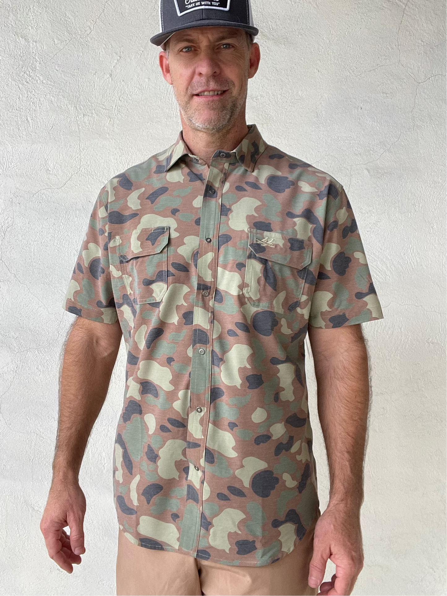 Man wearing a camouflage shirt and cap against a white wall
