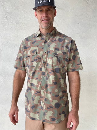 Man wearing a camouflage shirt and cap against a white wall