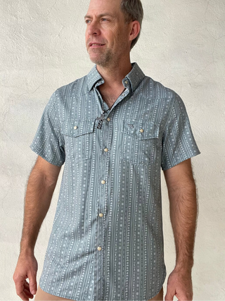 Man wearing a short-sleeve patterned shirt against a textured beige wall