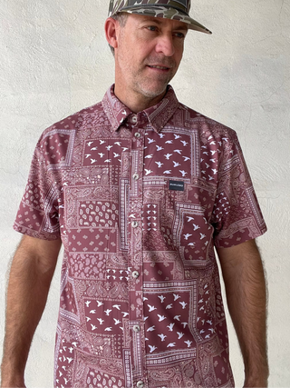 Man wearing a patterned shirt and camouflage cap against a plain background