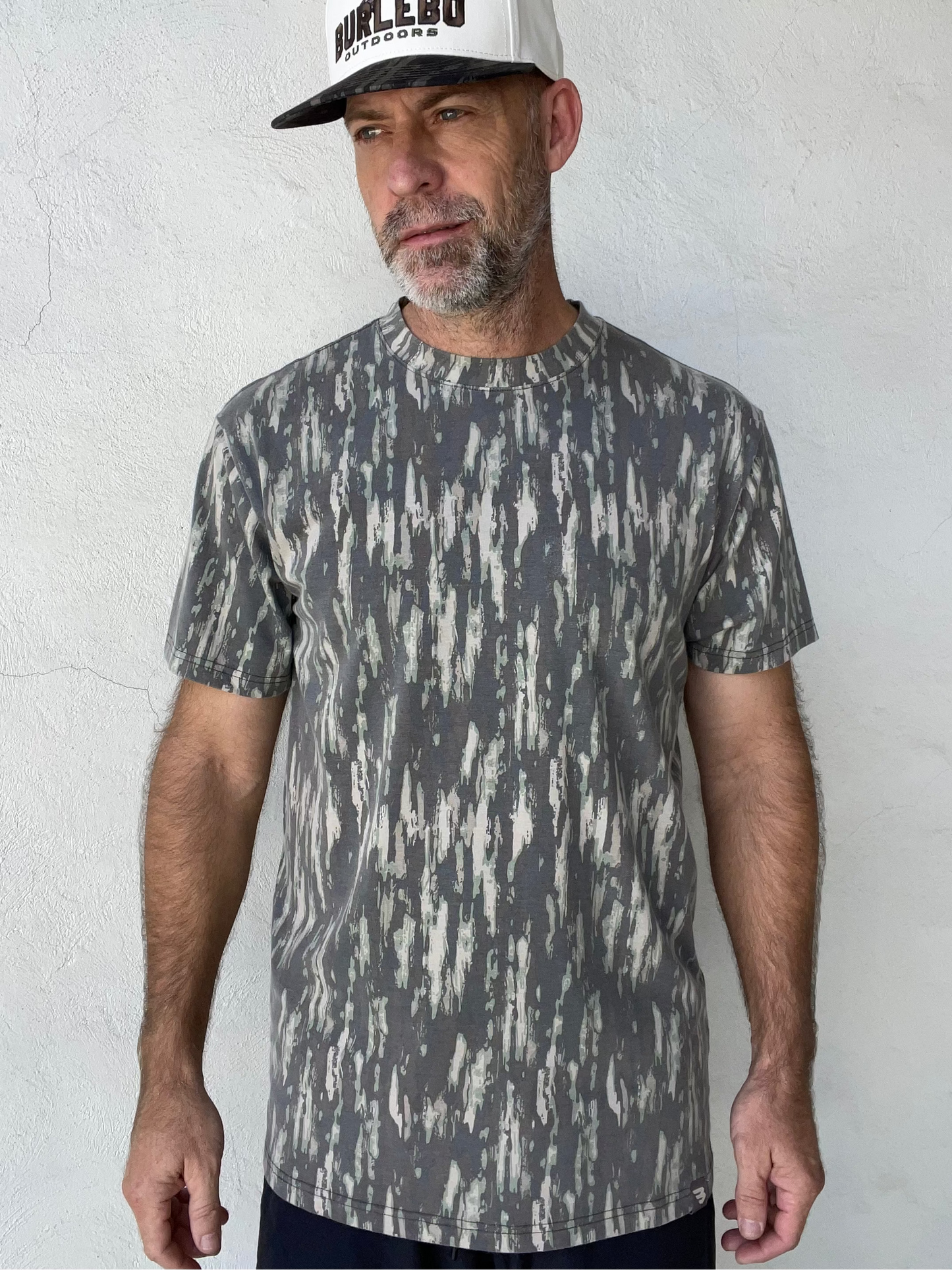 A man wearing a short-sleeve crewneck t-shirt with a gray and white distressed vertical pattern, paired with a white and black trucker hat that reads 'BURLEBO'.