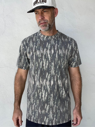 A man wearing a short-sleeve crewneck t-shirt with a gray and white distressed vertical pattern, paired with a white and black trucker hat that reads 'BURLEBO'.