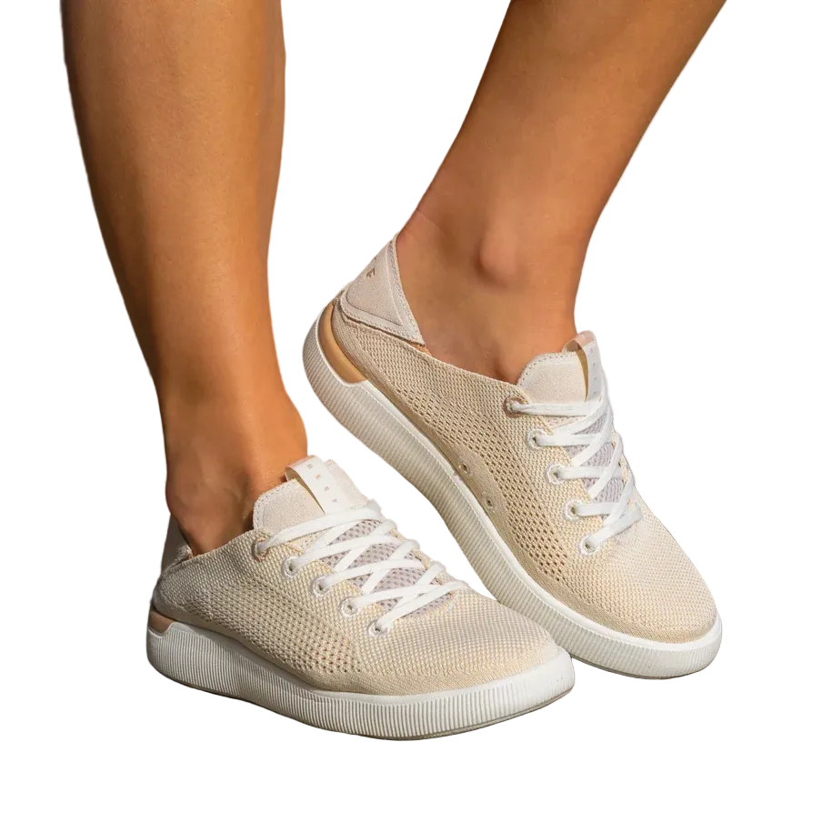 Beige sneakers with white laces worn by a person on a stone surface.