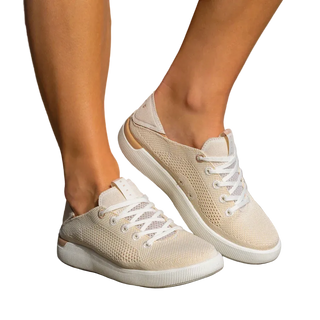 Beige sneakers with white laces worn by a person on a stone surface.