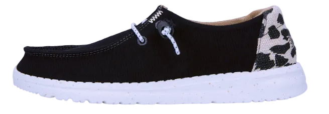 A women's casual shoe by HEYDUDE, featuring a black canvas upper with leopard print detailing on the heel and a white sole.