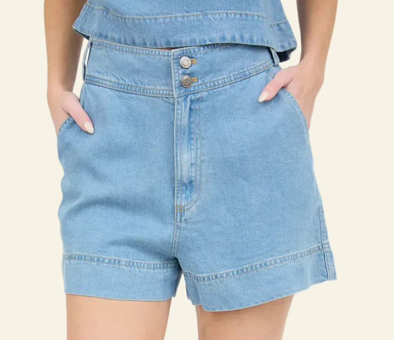 A pair of high-waisted blue chambray mini shorts with a double button and zipper closure, and belt loops.
