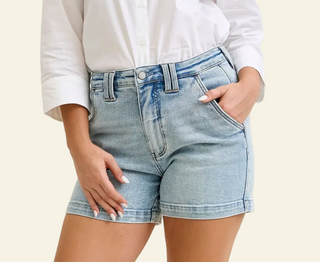 Person wearing light blue denim shorts and a white shirt on a beige background