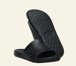 Black slide sandals with textured sole on a white background