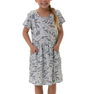 A young girl smiling and wearing a short-sleeve gray and white camouflage print dress with side pockets, standing against a plain white background.