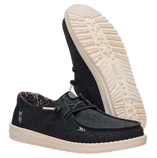 A pair of slip-on casual shoes with a dark black textured upper and cream-colored soles, shown with one shoe standing upright to display the treaded outsole.